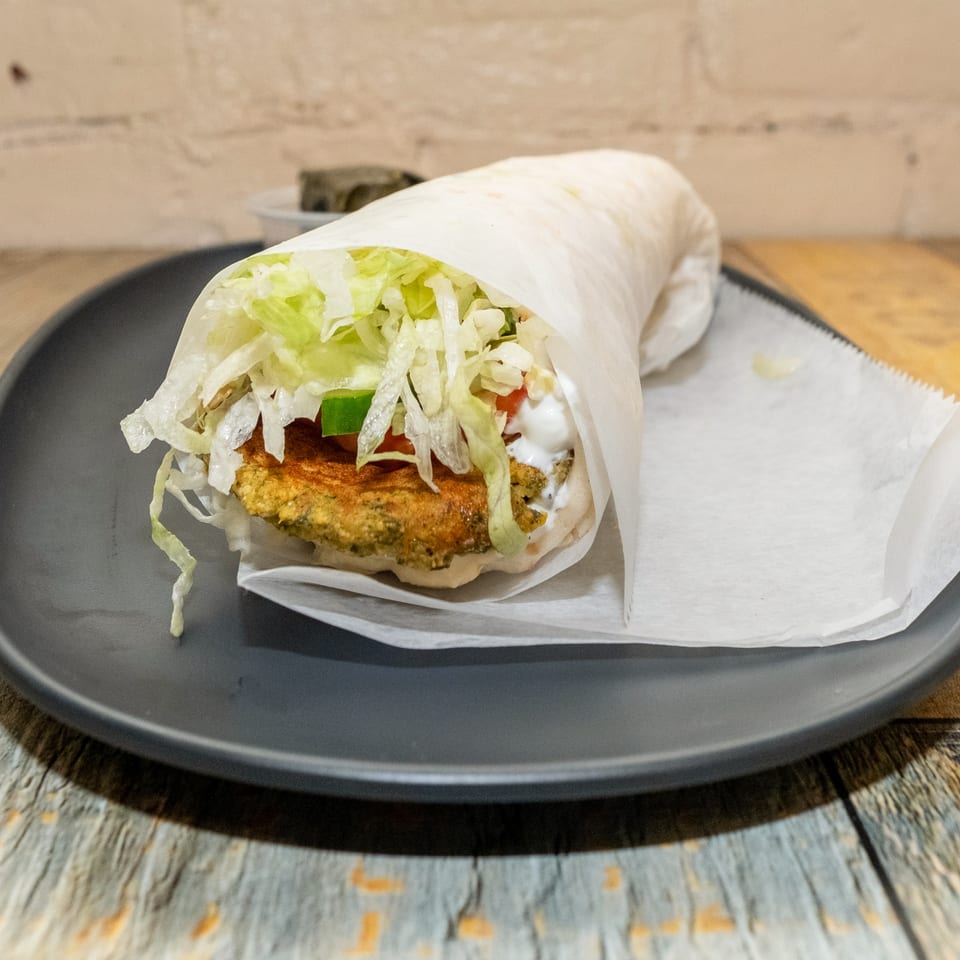 Falafel wrap with crisp lettuce, diced tomatoes, and creamy white sauce on a dark plate.