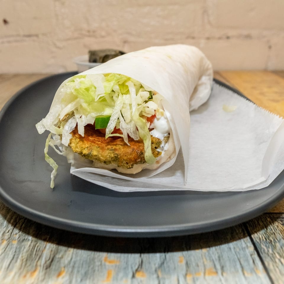 A falafel wrap with fresh lettuce, tomatoes, and creamy sauce on a dark plate.