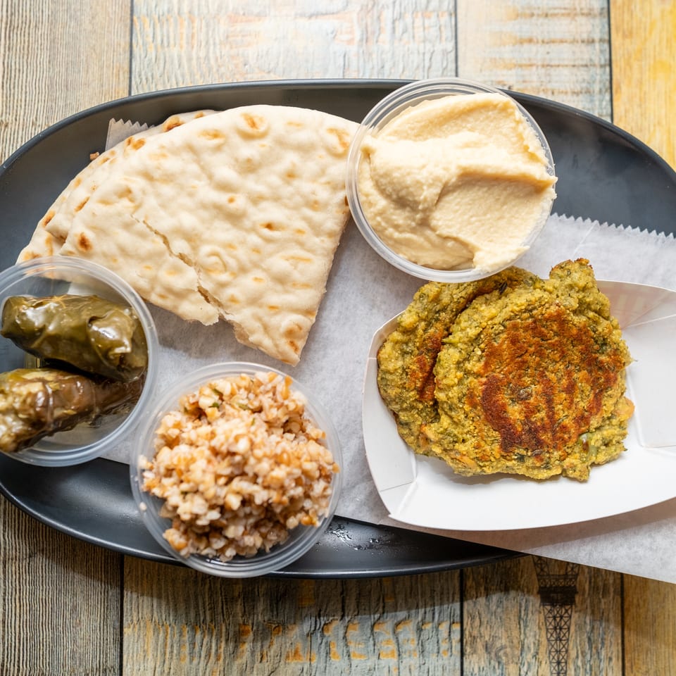Mediterranean platter with pita, hummus, grape leaves, grain salad, and falafel patties.