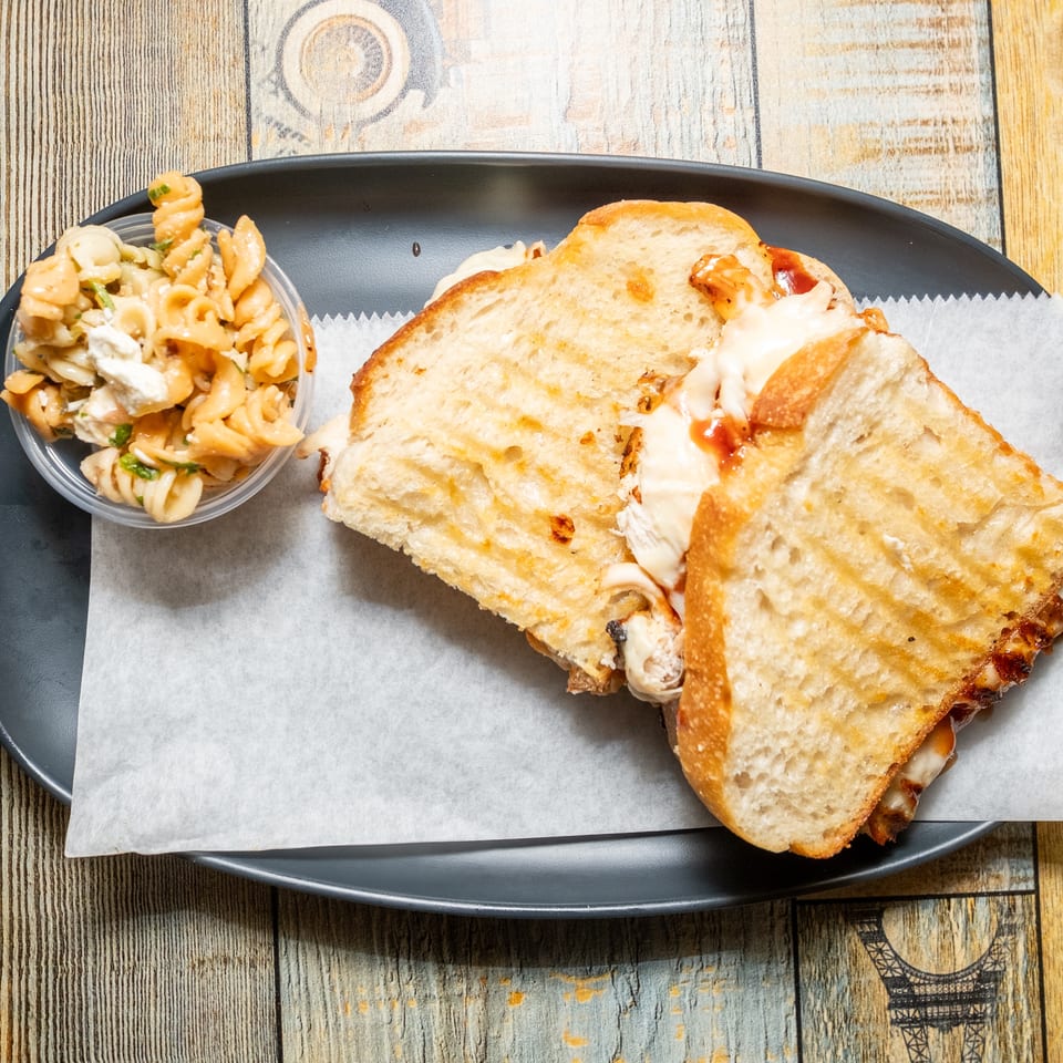 A grilled sandwich cut in half with melted cheese and a side of pasta salad.